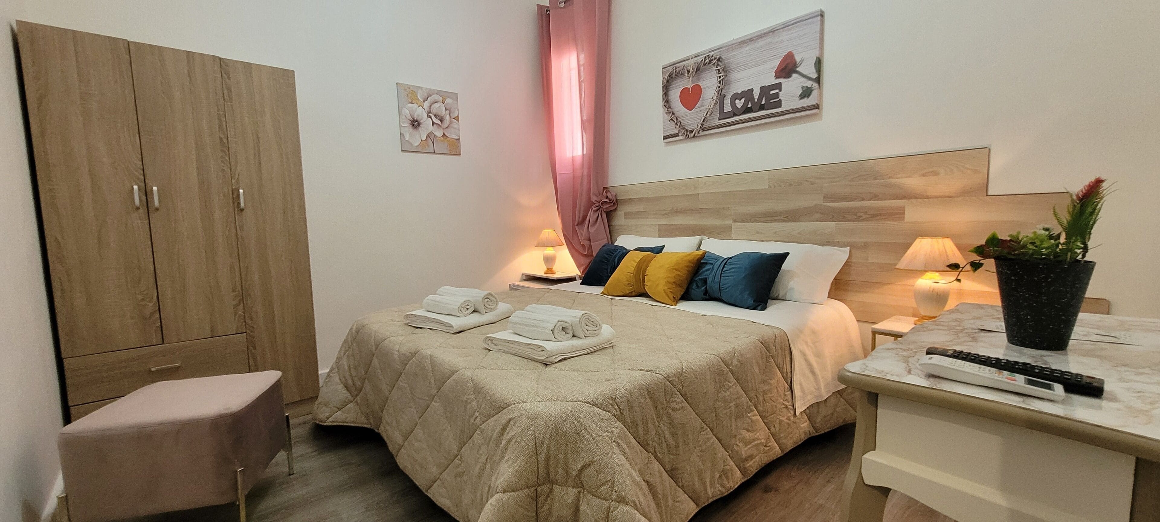 Un dormitorio ordenado con cama, mesitas de noche, un armario y un escritorio pequeño con un control remoto.