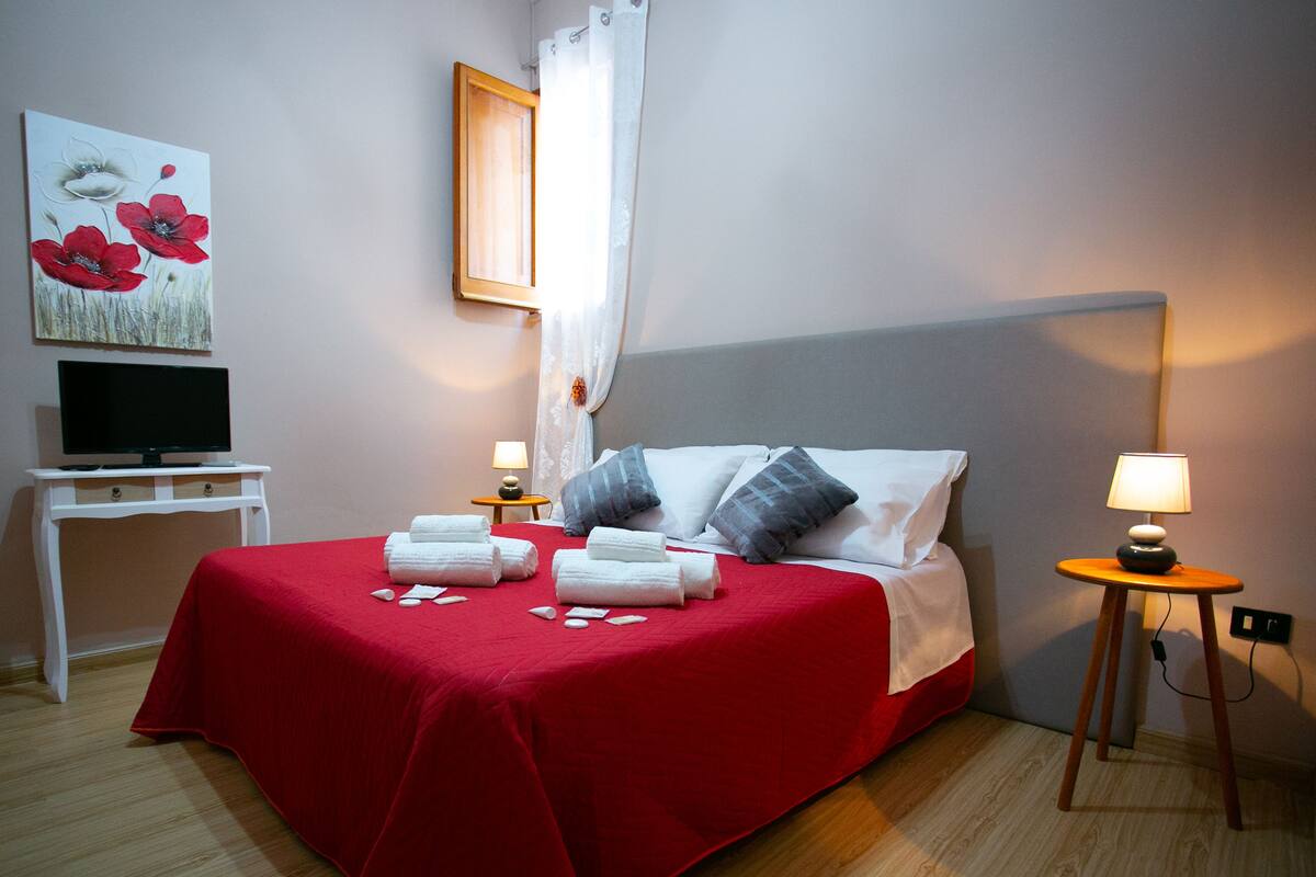 Una habitación de hotel con una cama, dos mesitas de noche, un televisor y un cuadro en la pared.
