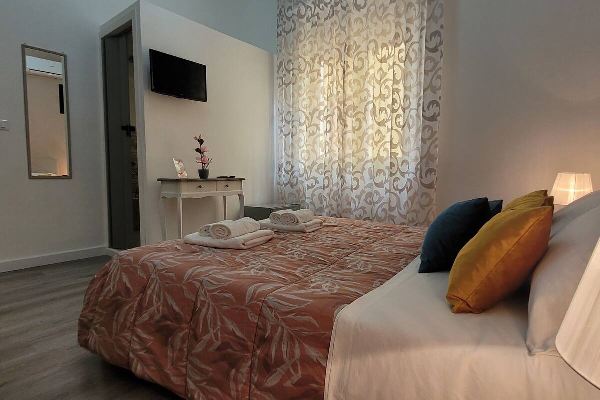 Una habitación de hotel con cama, escritorio, televisor y ventana con cortinas.