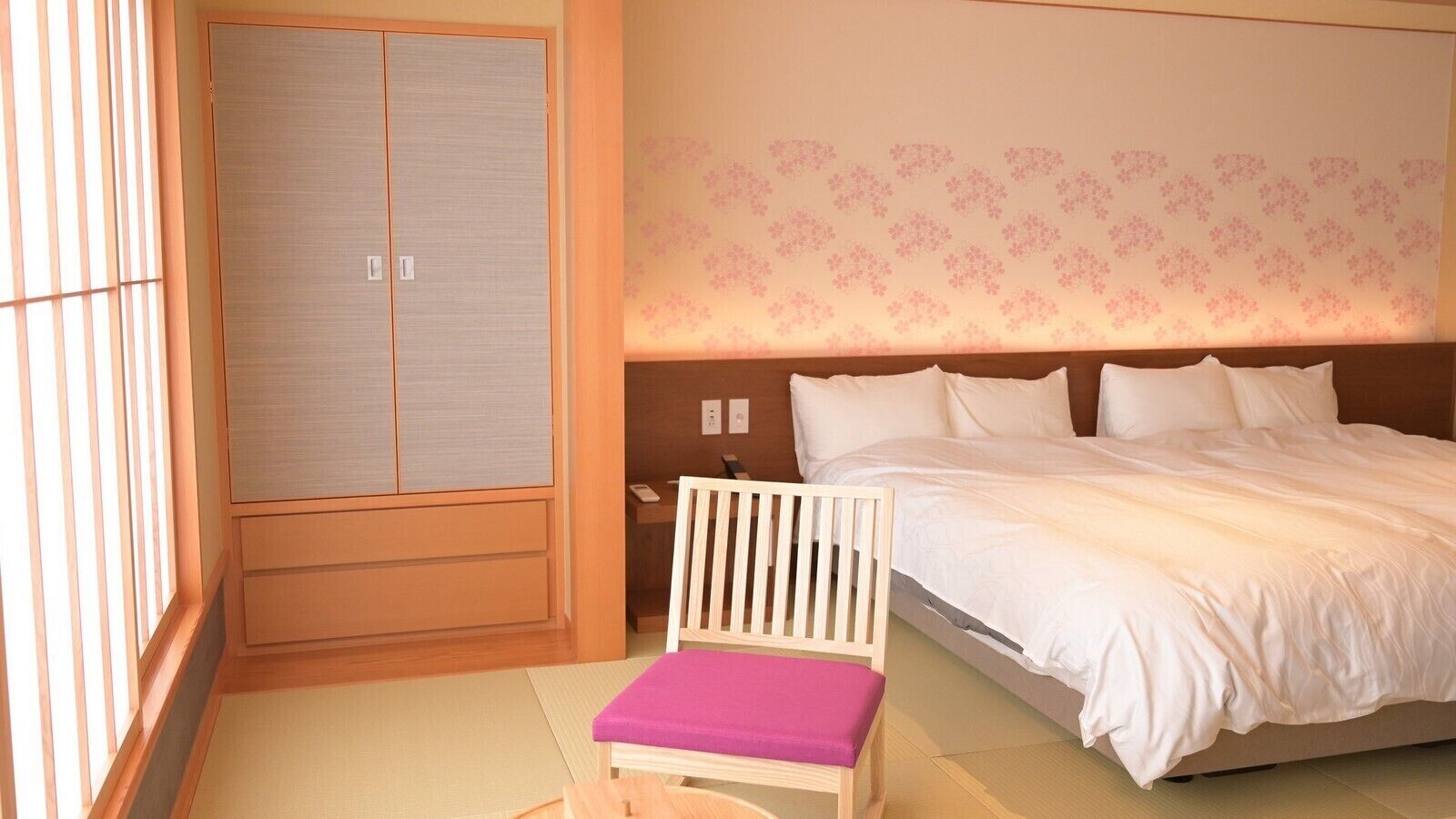 A bedroom with a bed, a chair, a wardrobe, and a wall with a floral pattern.