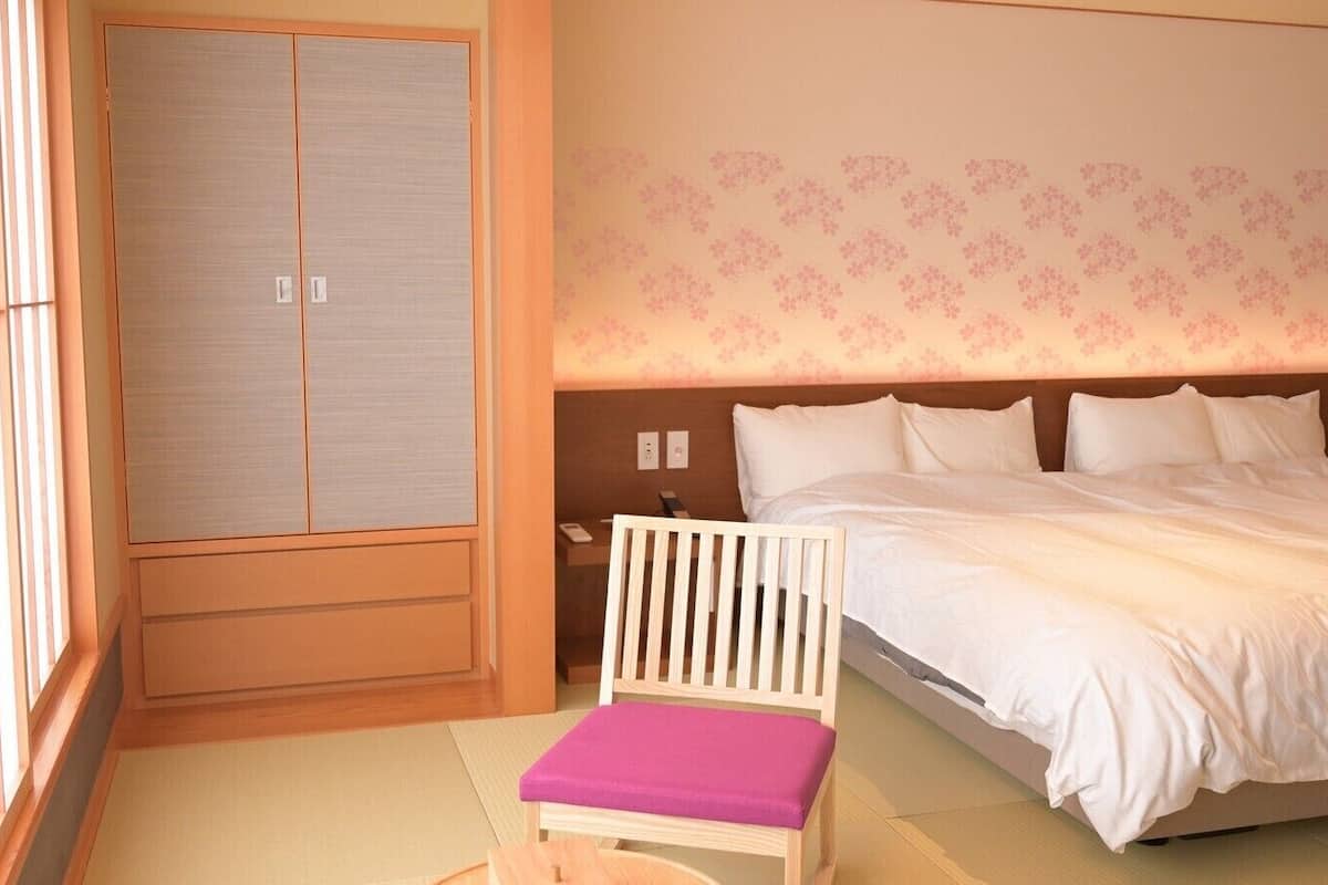 Ein Schlafzimmer mit Bett, Stuhl, Kleiderschrank und einer Wand mit Blumenmuster.