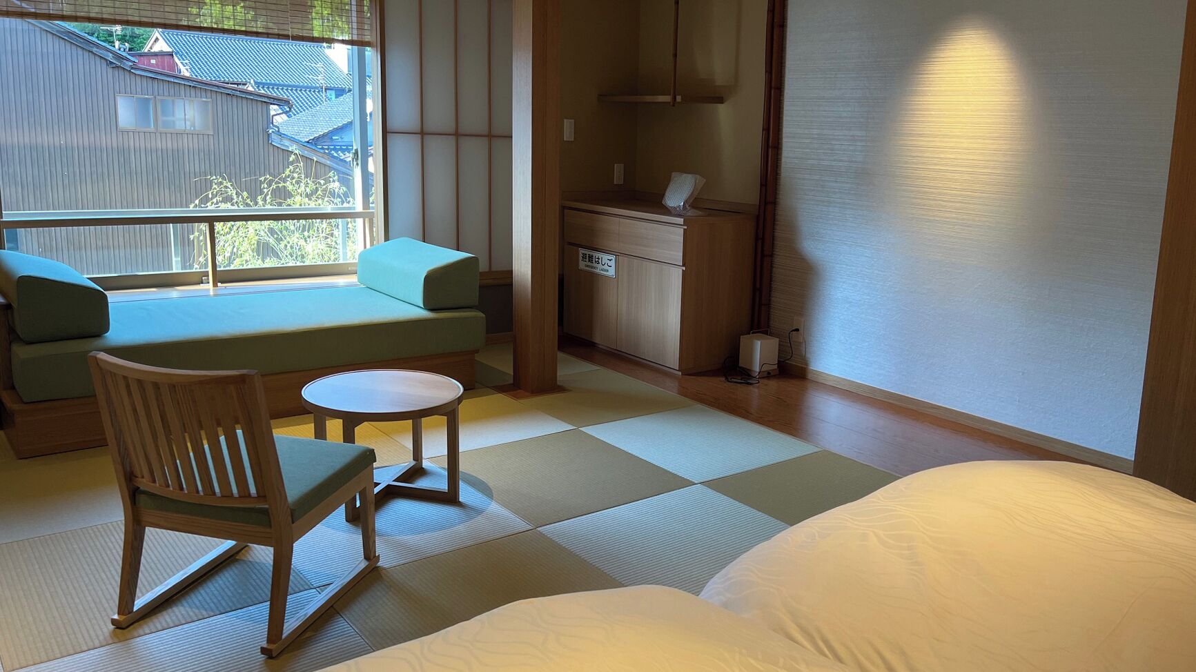 A traditional Japanese room with tatami flooring, a low table, a cushioned bench, and a bed.