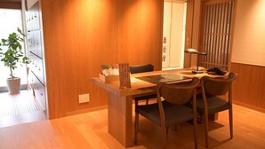 A wooden dining table with chairs, a potted plant, and a small cabinet with items on it.