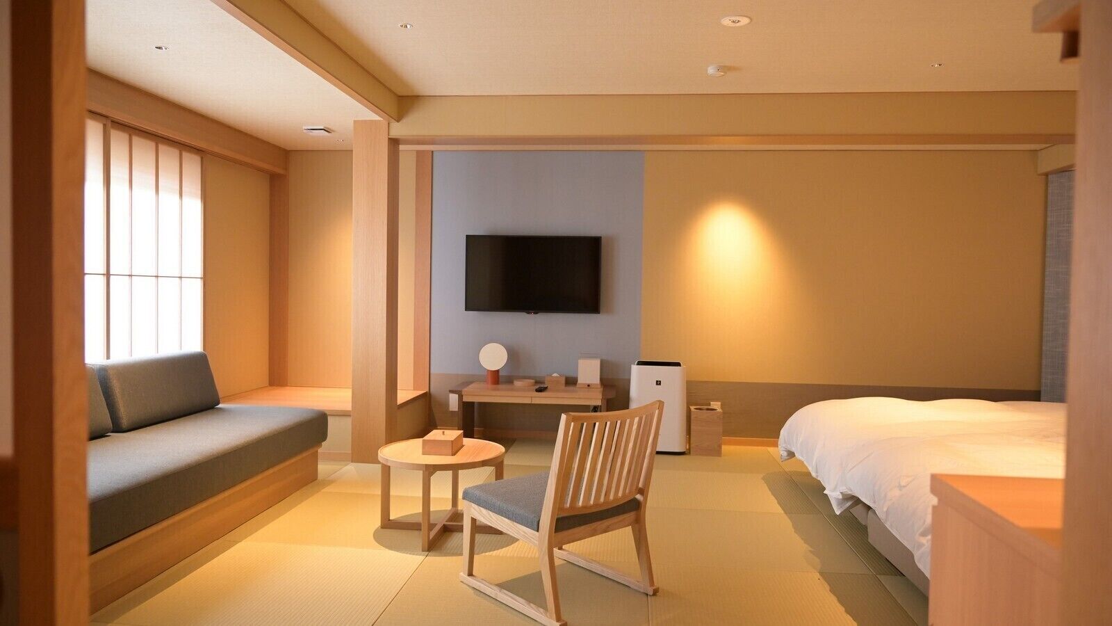 A hotel room with a sofa, a bed, a TV, a small table, and a chair.