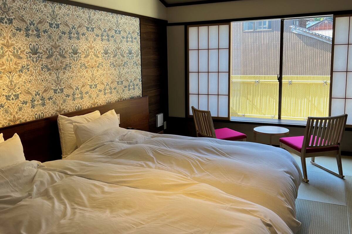 Ein Hotelzimmer mit einem großen Bett, einer traditionellen japanischen Schiebetür und einem kleinen Tisch mit Stühlen.
