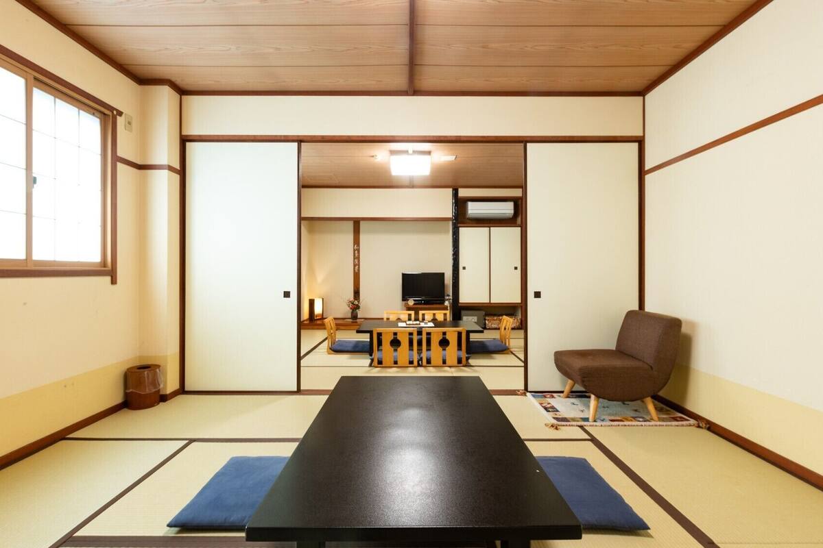 A traditional Japanese room with tatami flooring, a low table, a television, and a chair.