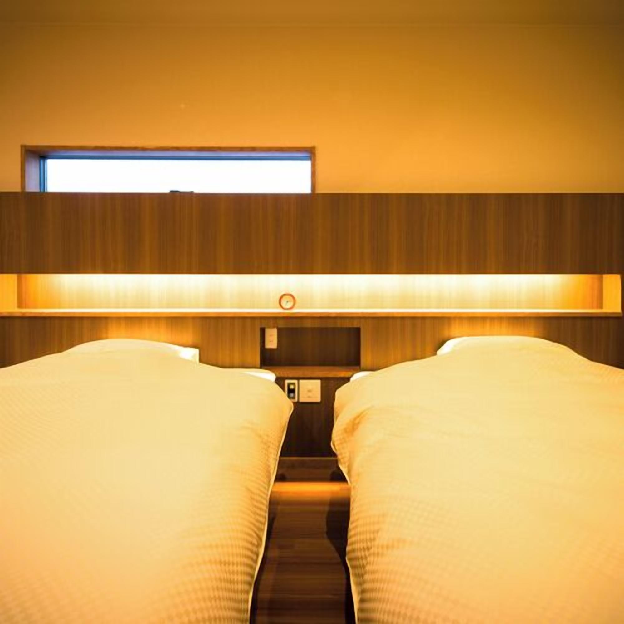 A hotel room with two beds, a window, and a wall-mounted control panel.