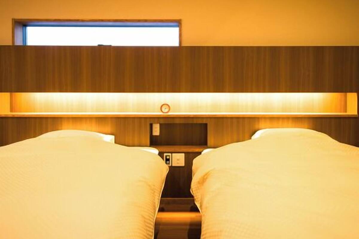 A hotel room with two beds, a window, and a wall-mounted control panel.