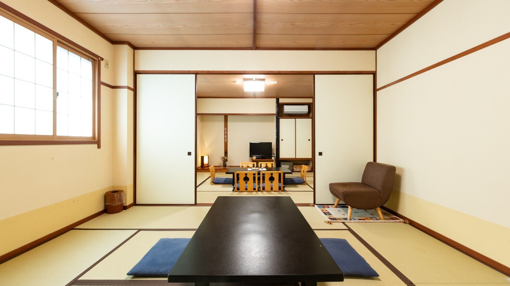 Une pièce de style japonais traditionnel, avec un sol recouvert de tatamis, une table basse, un téléviseur et une chaise.
