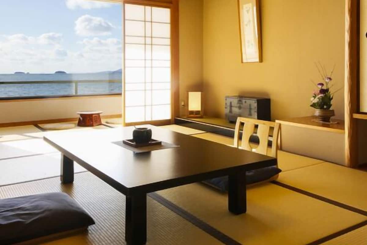A traditional Japanese room with tatami flooring, a low table, a sofa, and a view of the sea.