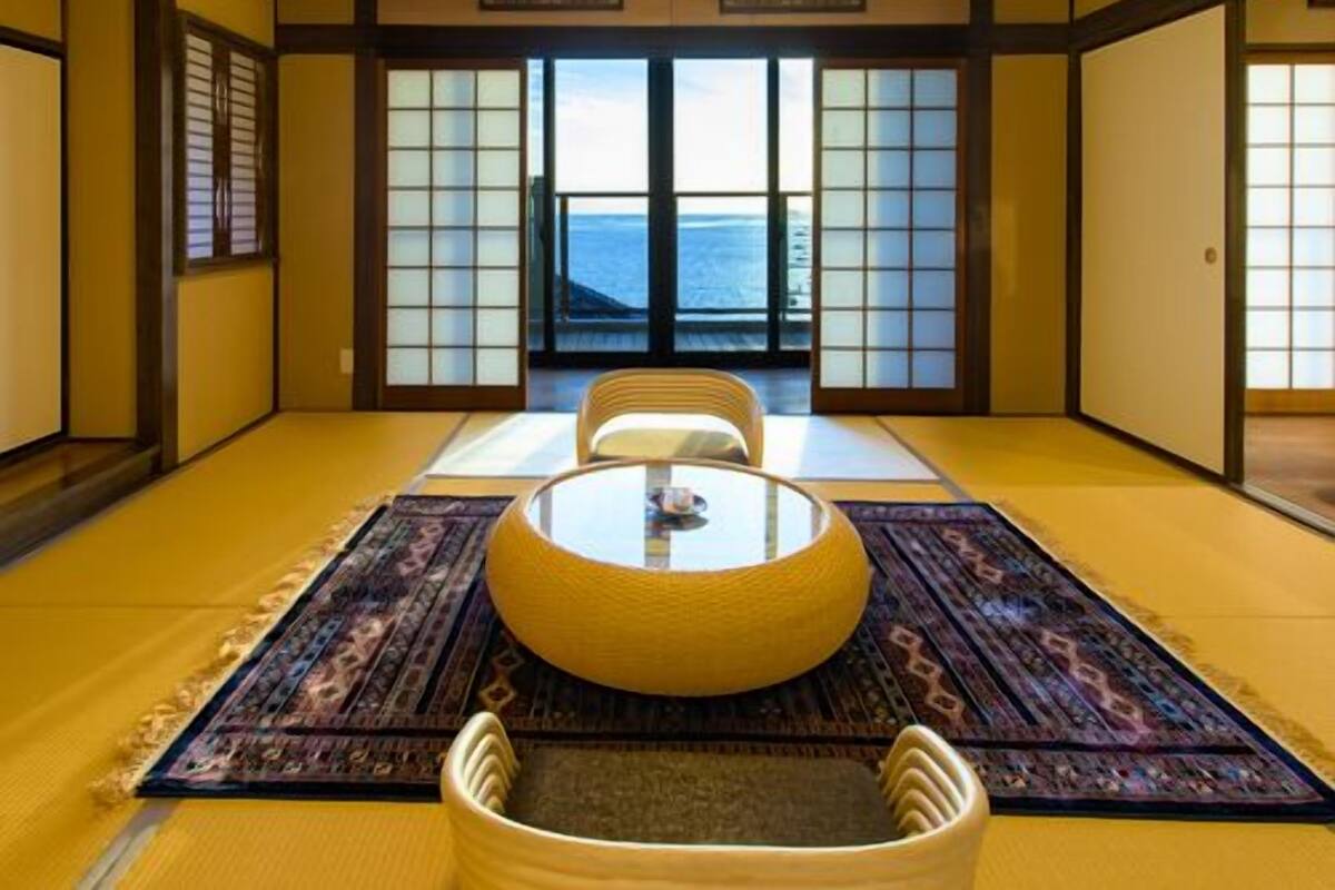 A traditional Japanese room with tatami flooring, a low table with cushions, and a view of the sea through shoji screens.