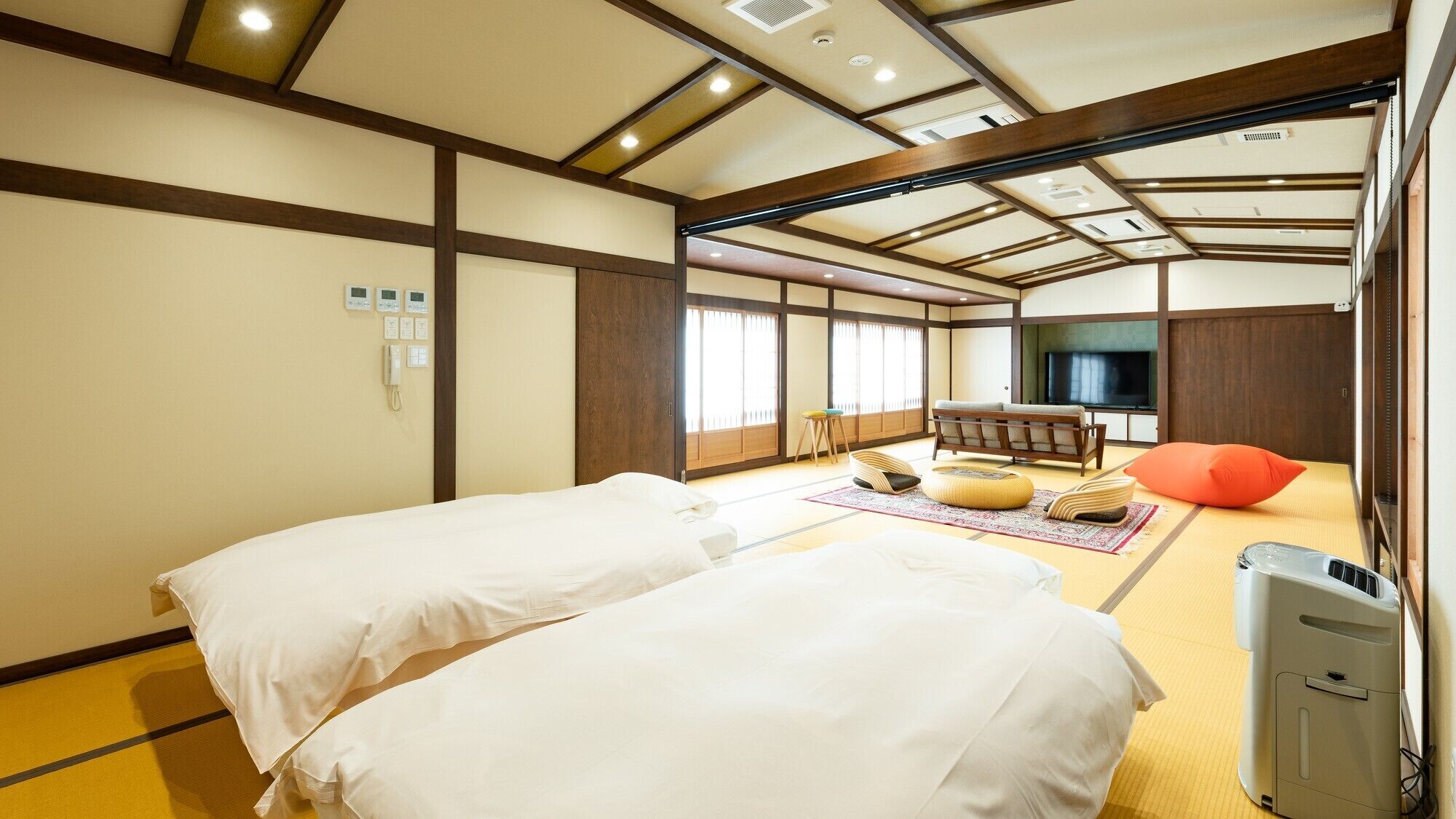 A traditional Japanese-style room with tatami flooring, two beds, a TV, and a futon.
