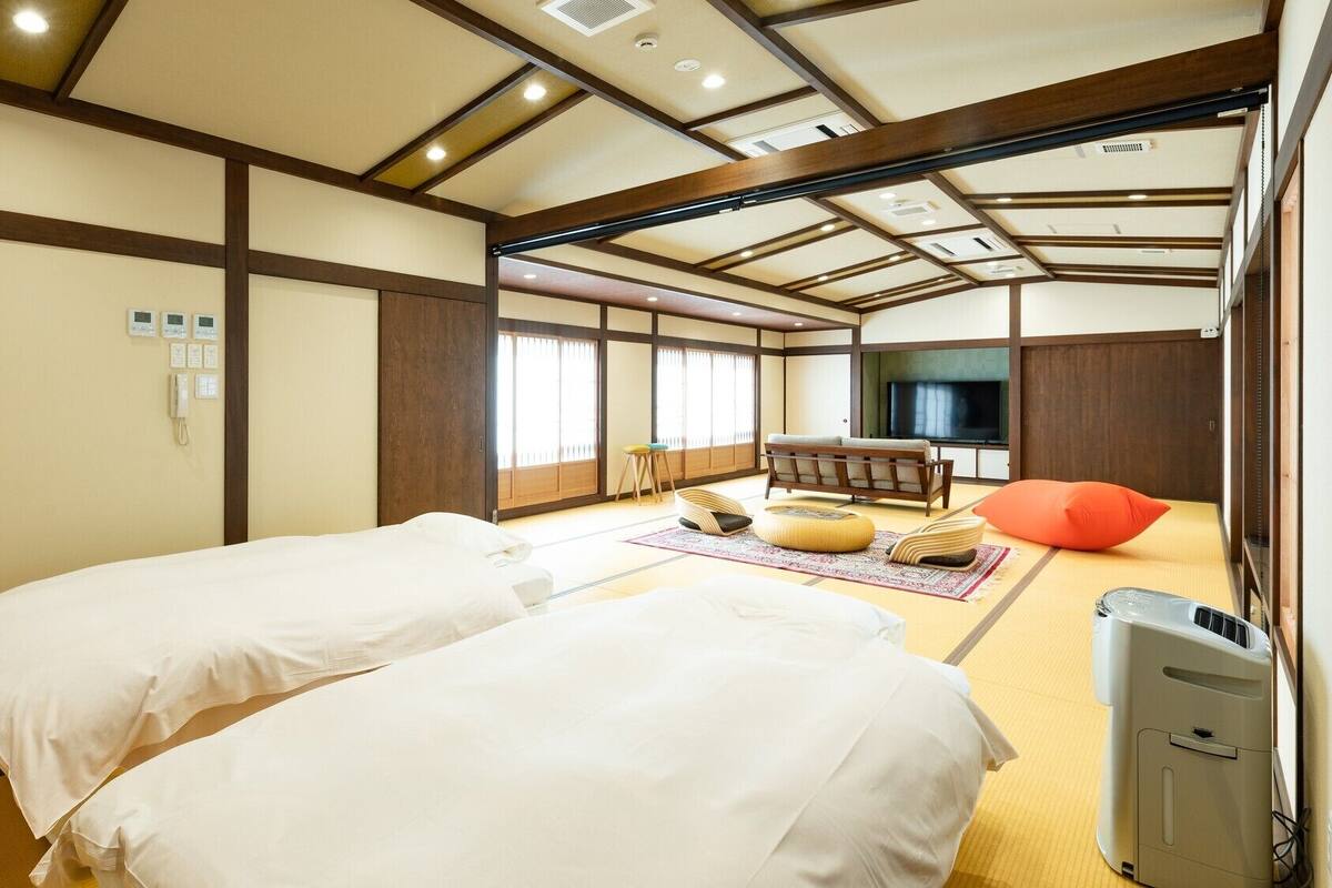 A traditional Japanese-style room with tatami flooring, two beds, a TV, and a futon.