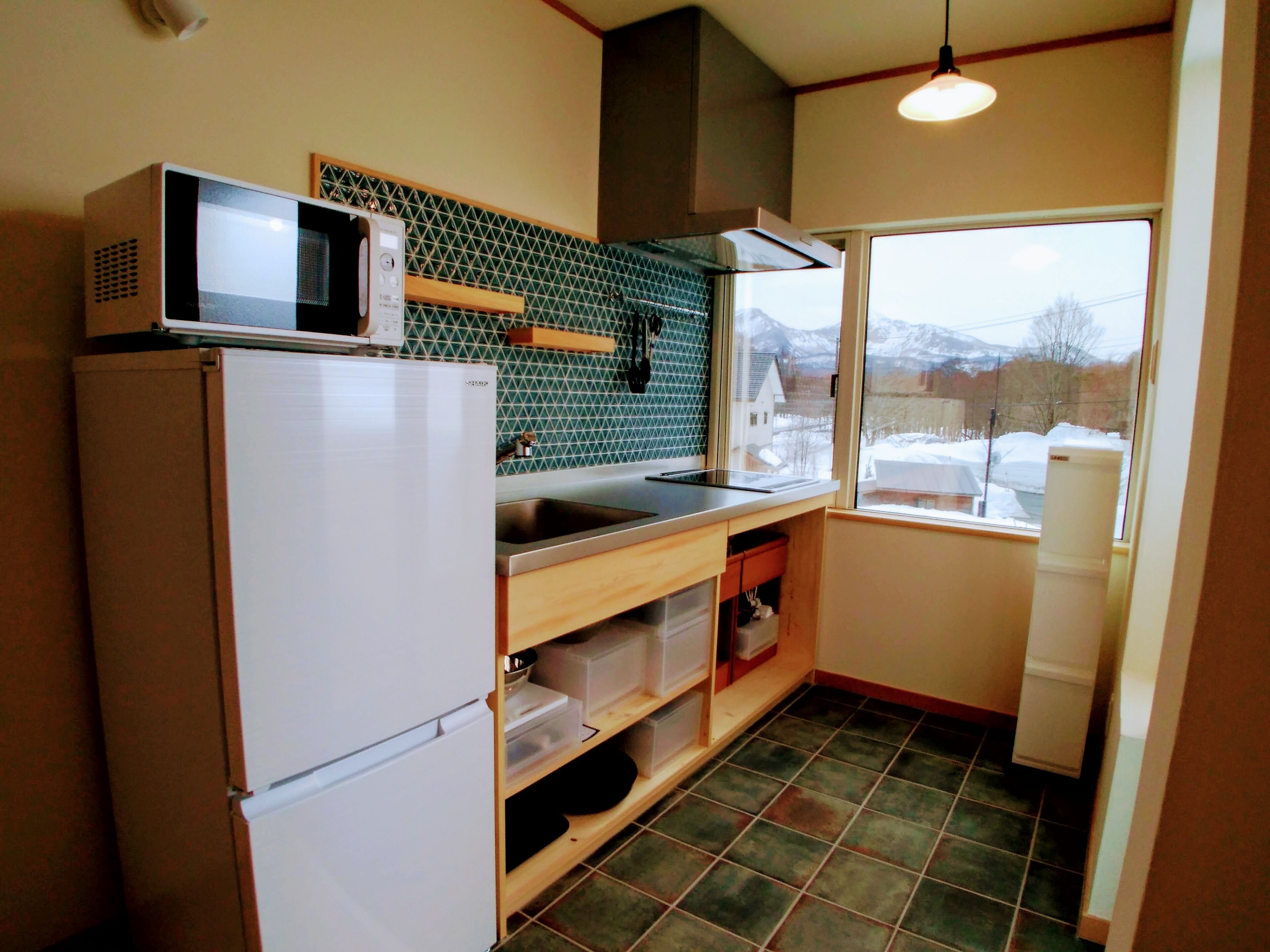 A compact kitchen with a microwave, refrigerator, and a window with a view of snow-covered mountains.