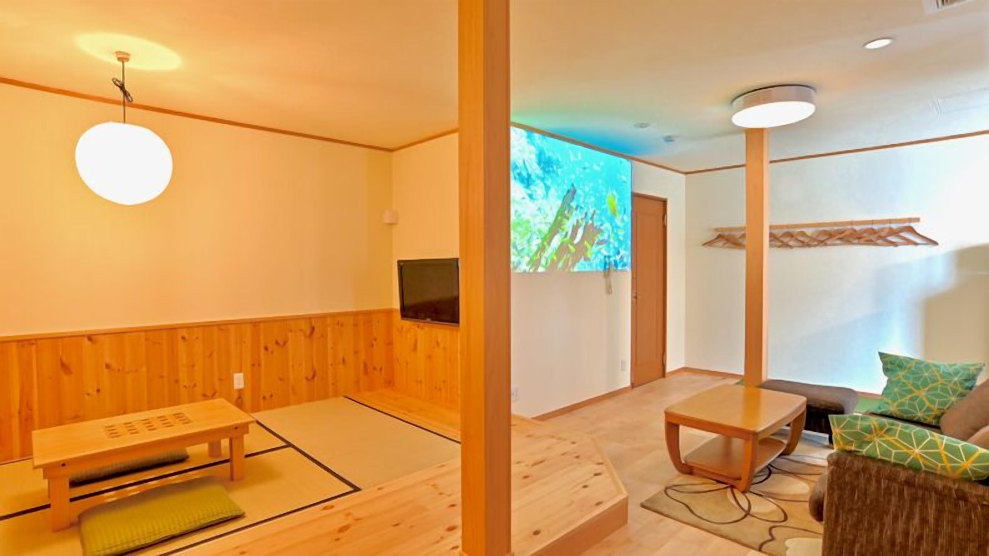 A traditional Japanese room with tatami flooring, a low table, a sofa with cushions, a television, and a projection screen.