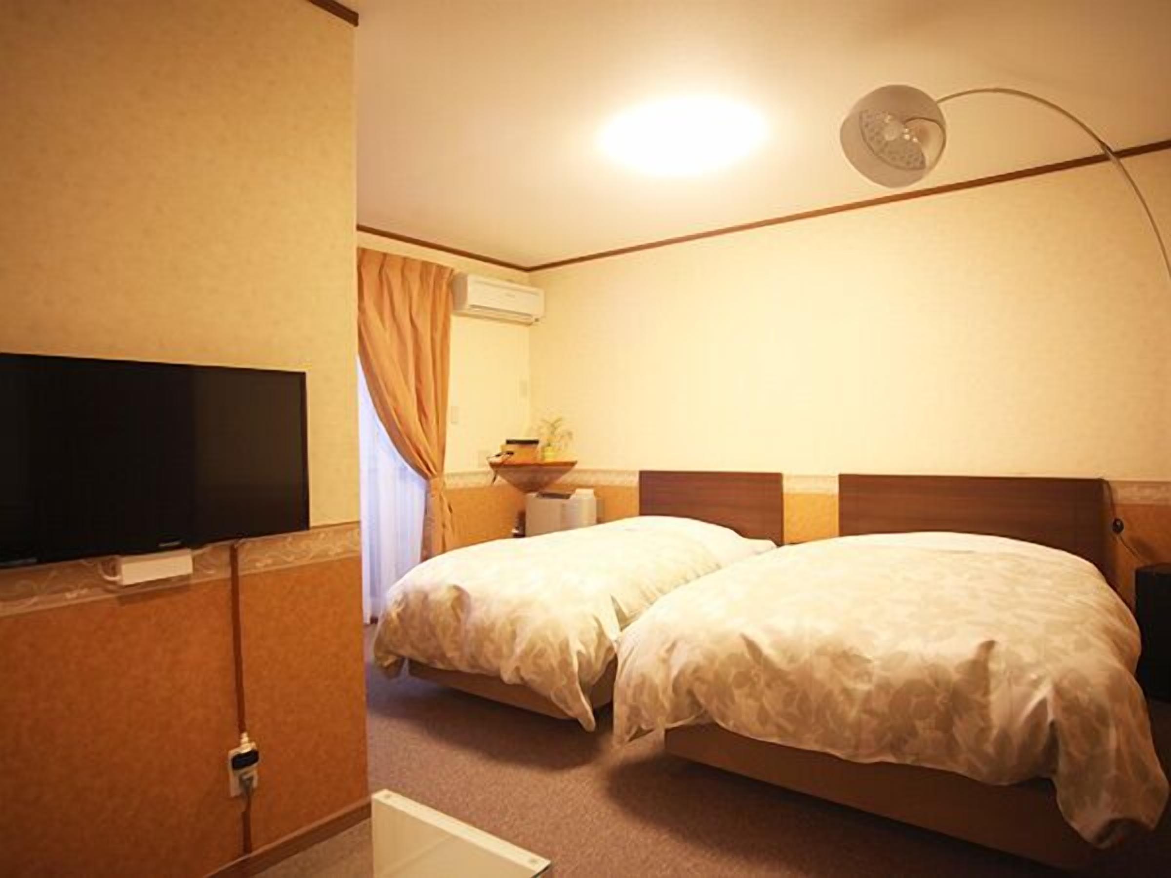 A hotel room with two beds, a television, a bedside table, and a ceiling light.
