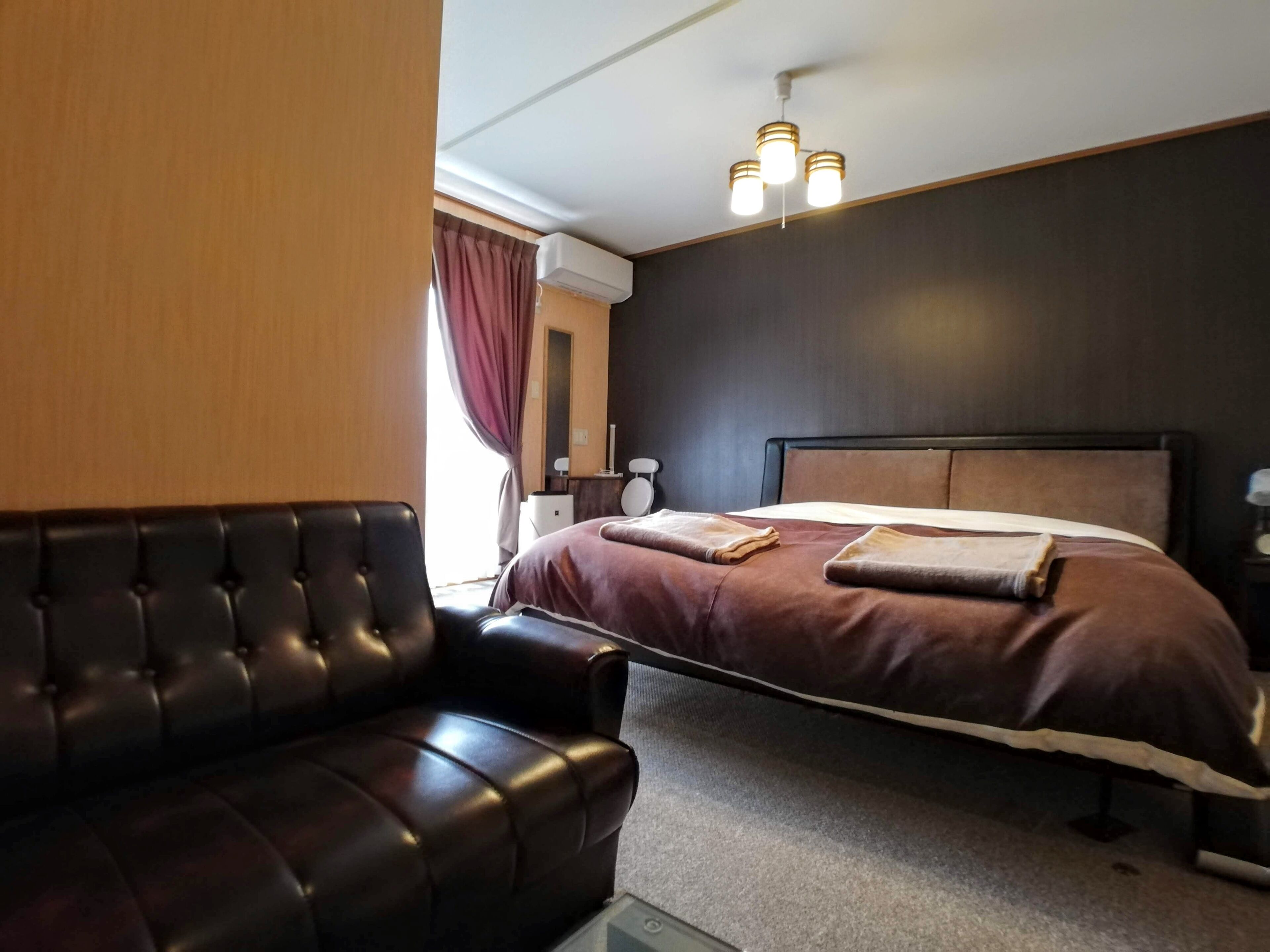 A bedroom with a bed, a leather sofa, a bedside table, and a ceiling light fixture.