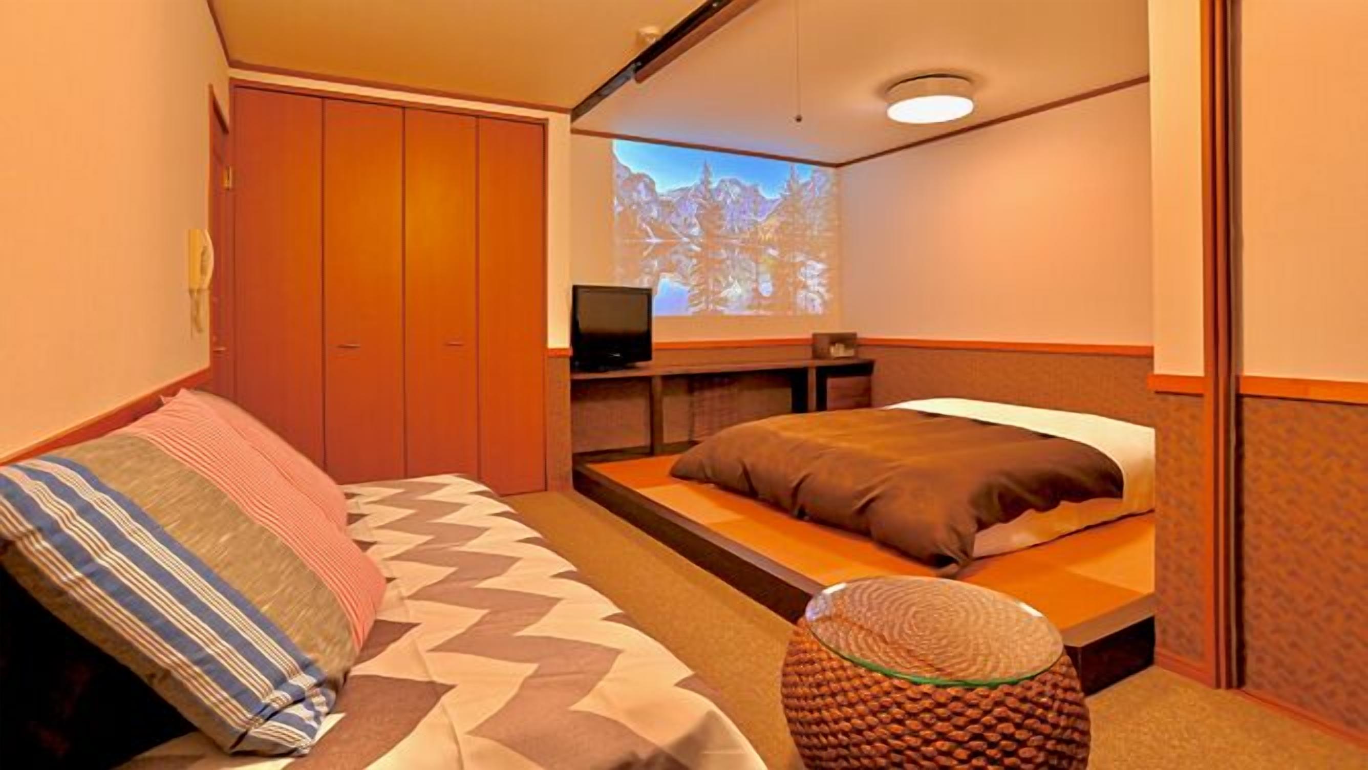 A hotel room with a bed, a television, a wardrobe, and a projection screen.