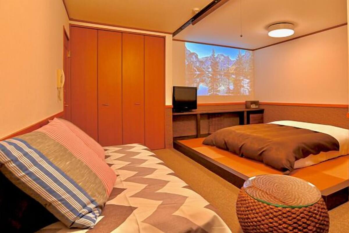 Ein Hotelzimmer mit Bett, Fernseher, Kleiderschrank und einer Projektionsleinwand.