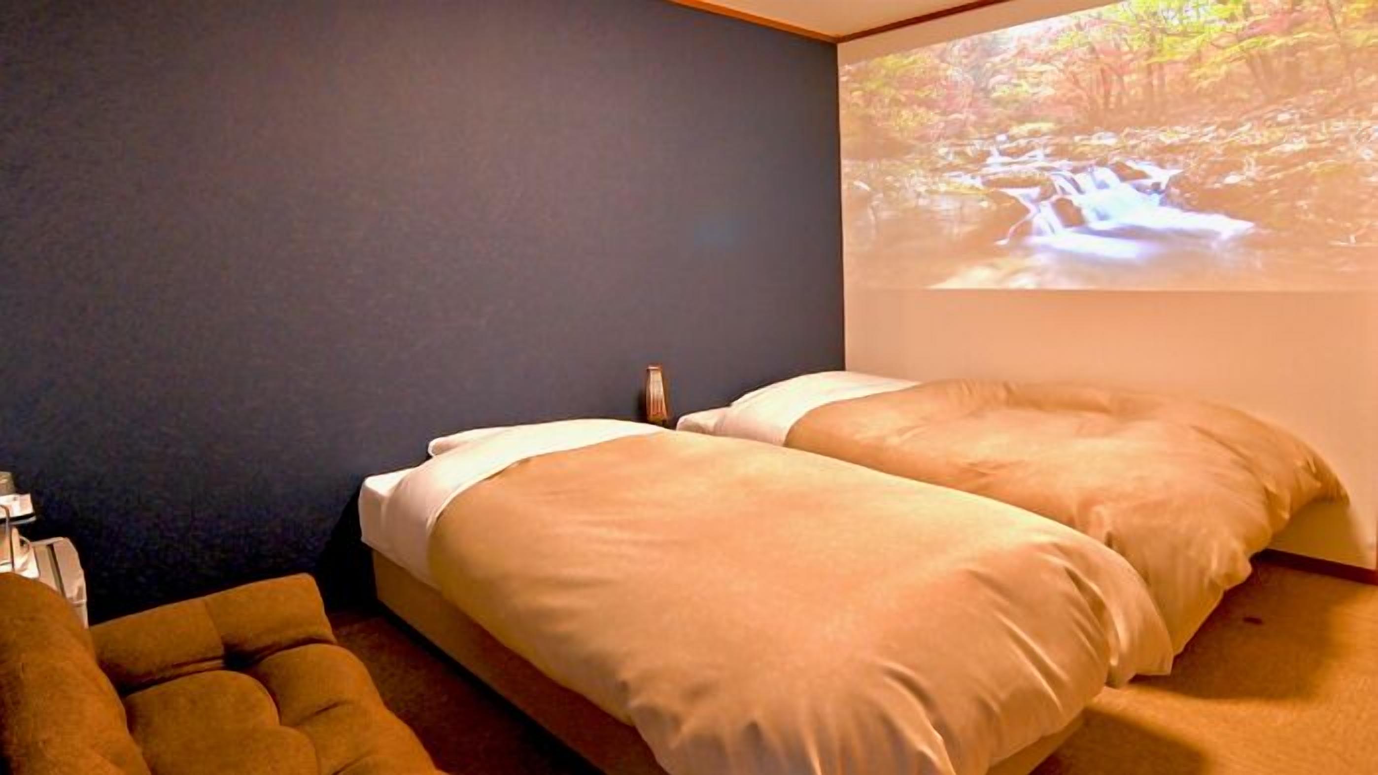 A bedroom with two beds, a small table, and a wall-mounted projector displaying a nature scene.