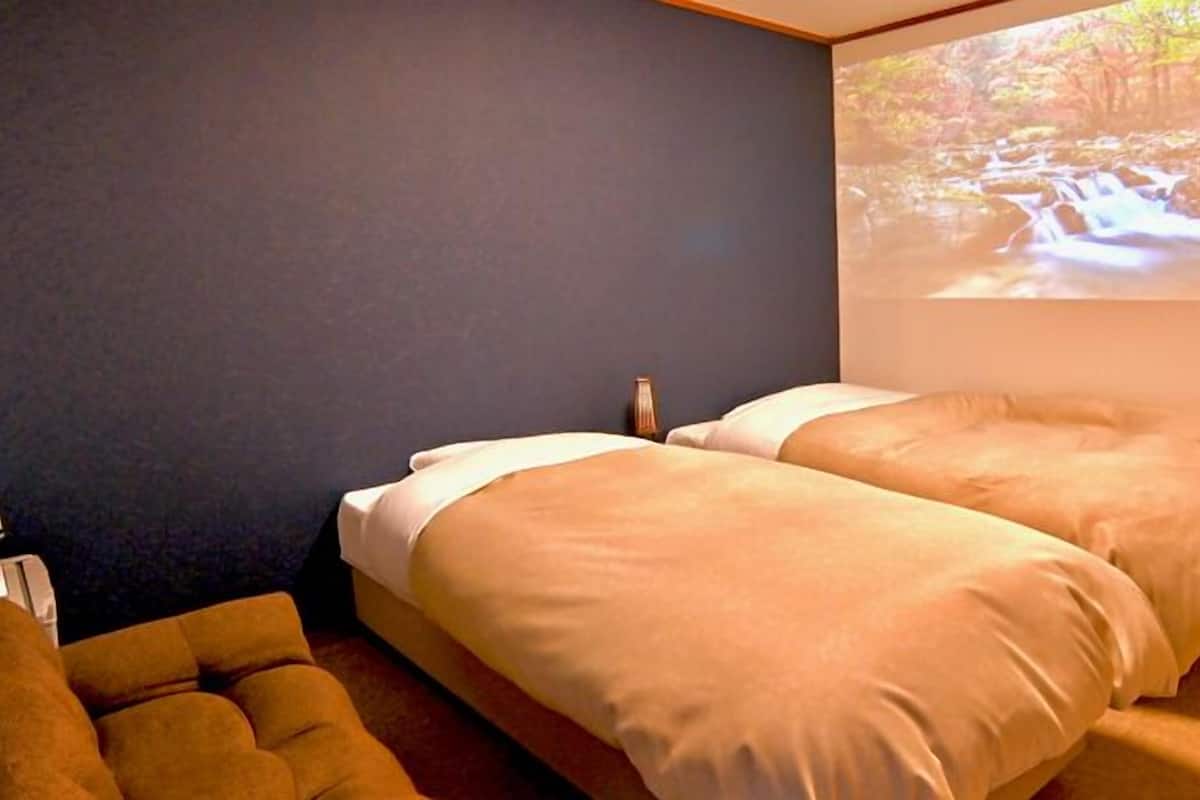 Ein Schlafzimmer mit zwei Betten, einem kleinen Tisch und einem an der Wand montierten Projektor, der eine Naturansicht zeigt.