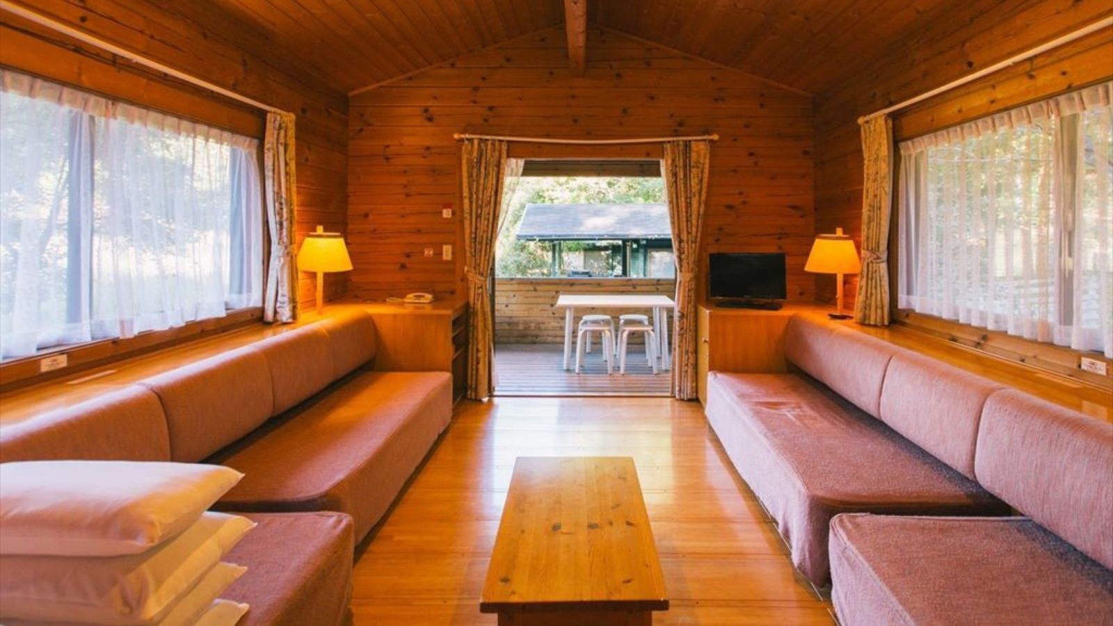 A cozy cabin interior with wooden walls, a central sofa, two side sofas, a wooden coffee table, and two lamps.