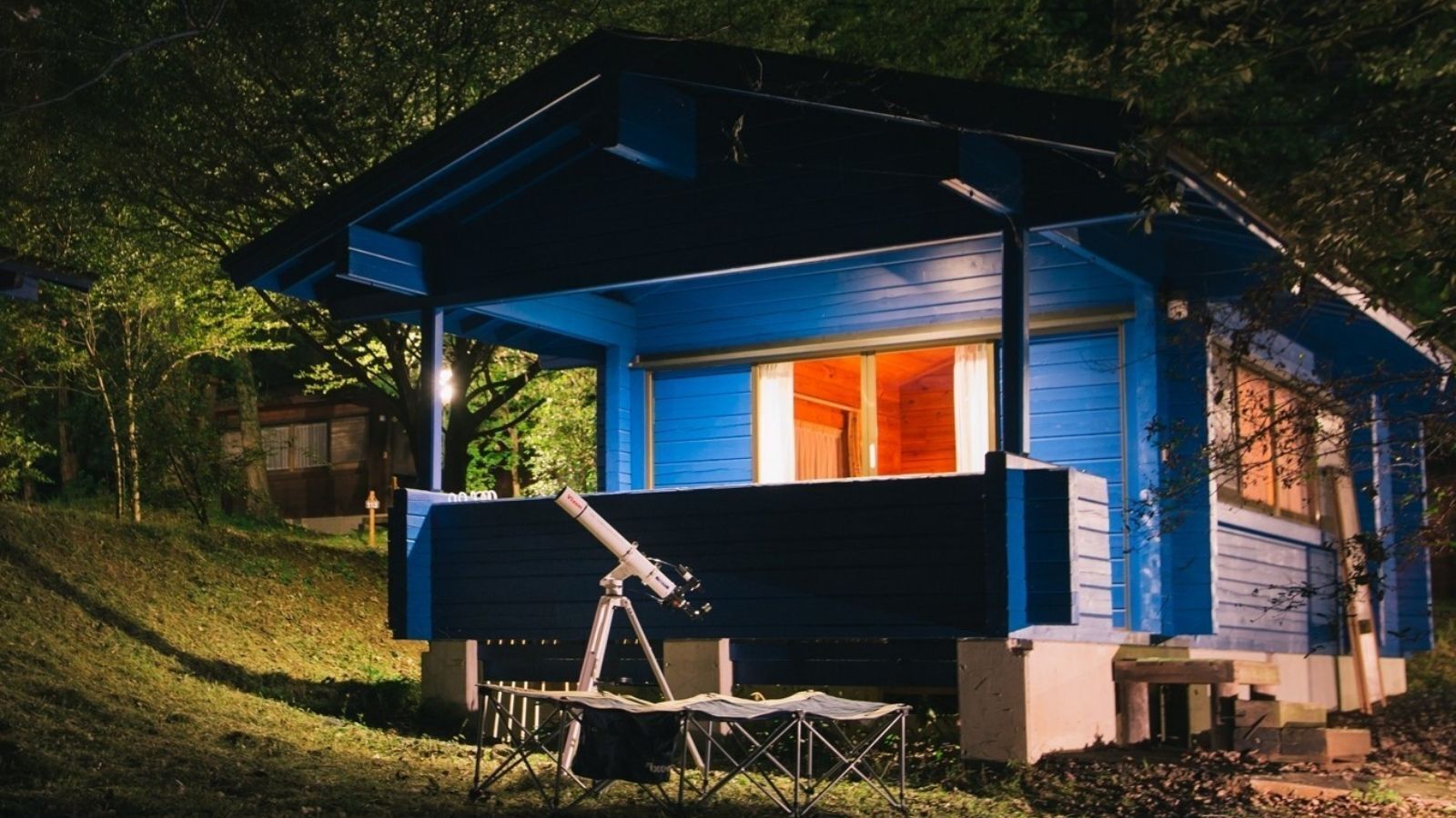 A small, single-story cabin with a porch and a telescope.