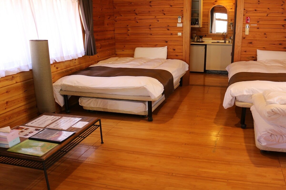 A cabin-style room with two beds, a small kitchenette, and a wooden floor.