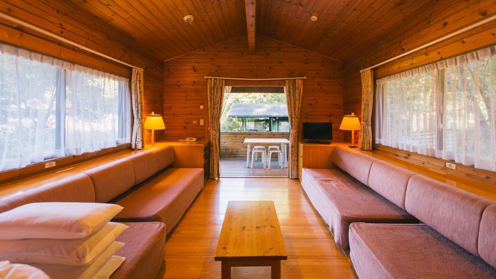 A cabin interior with wooden walls, a sofa, a table, and a TV.