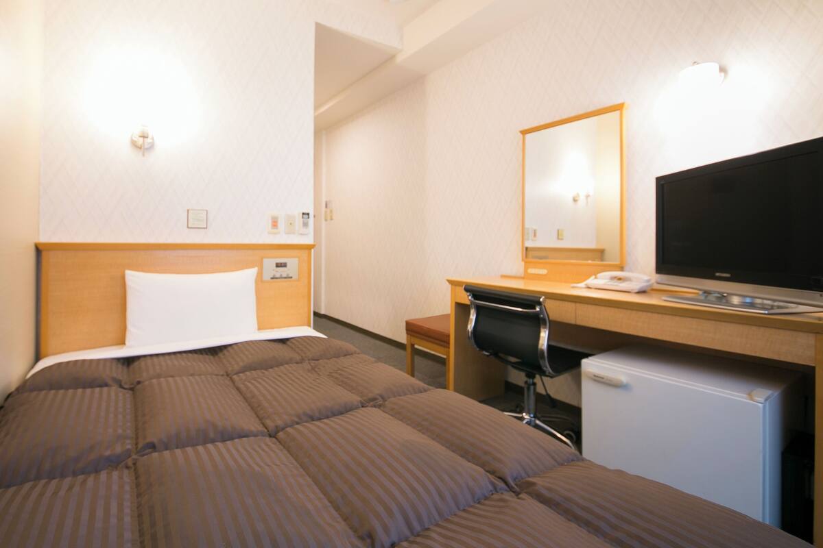 Une chambre d’hôtel équipée d’un lit, d’un bureau avec un ordinateur, d’une chaise et d’un petit réfrigérateur.