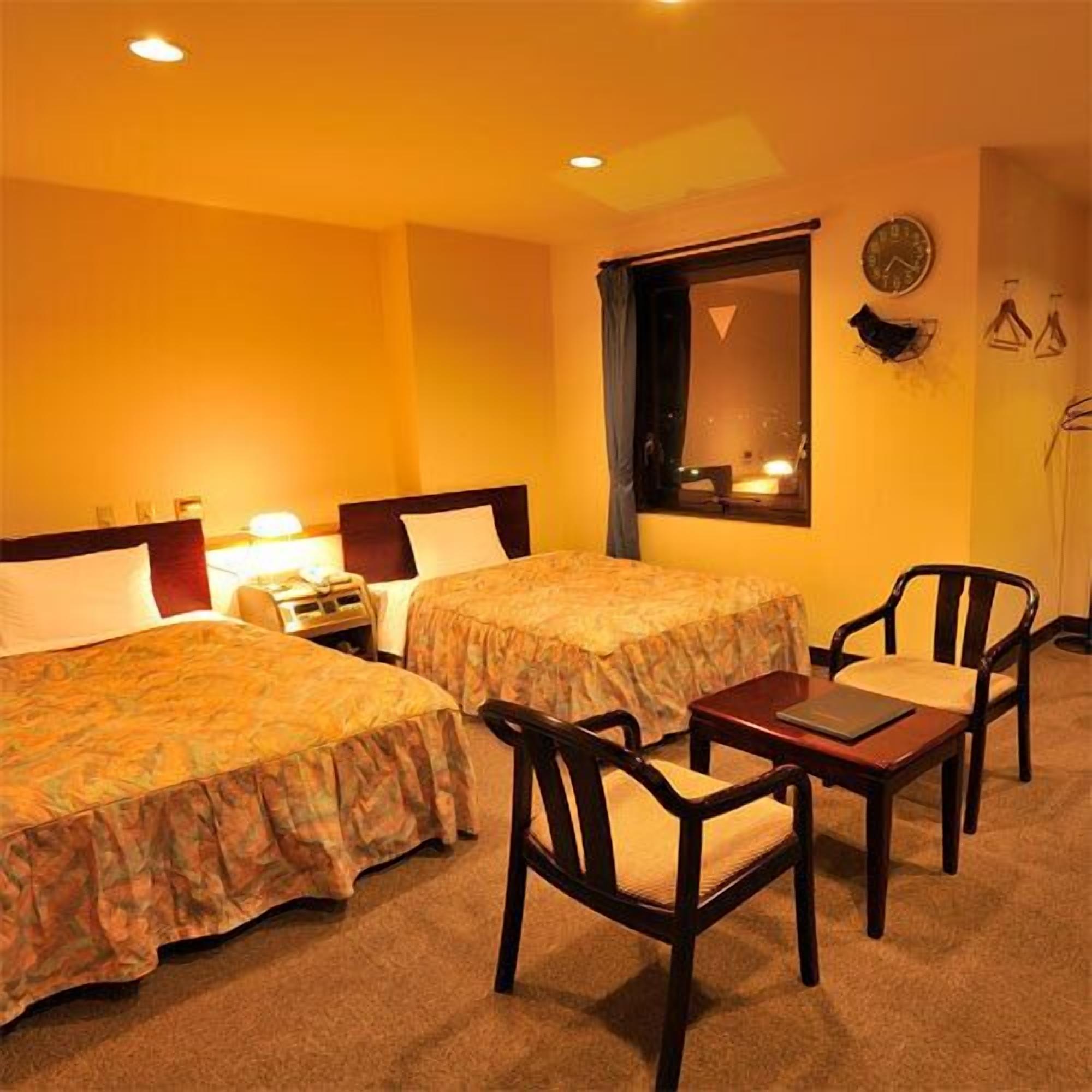 A hotel room with two beds, a desk with a chair, and a window with a view of the outside.