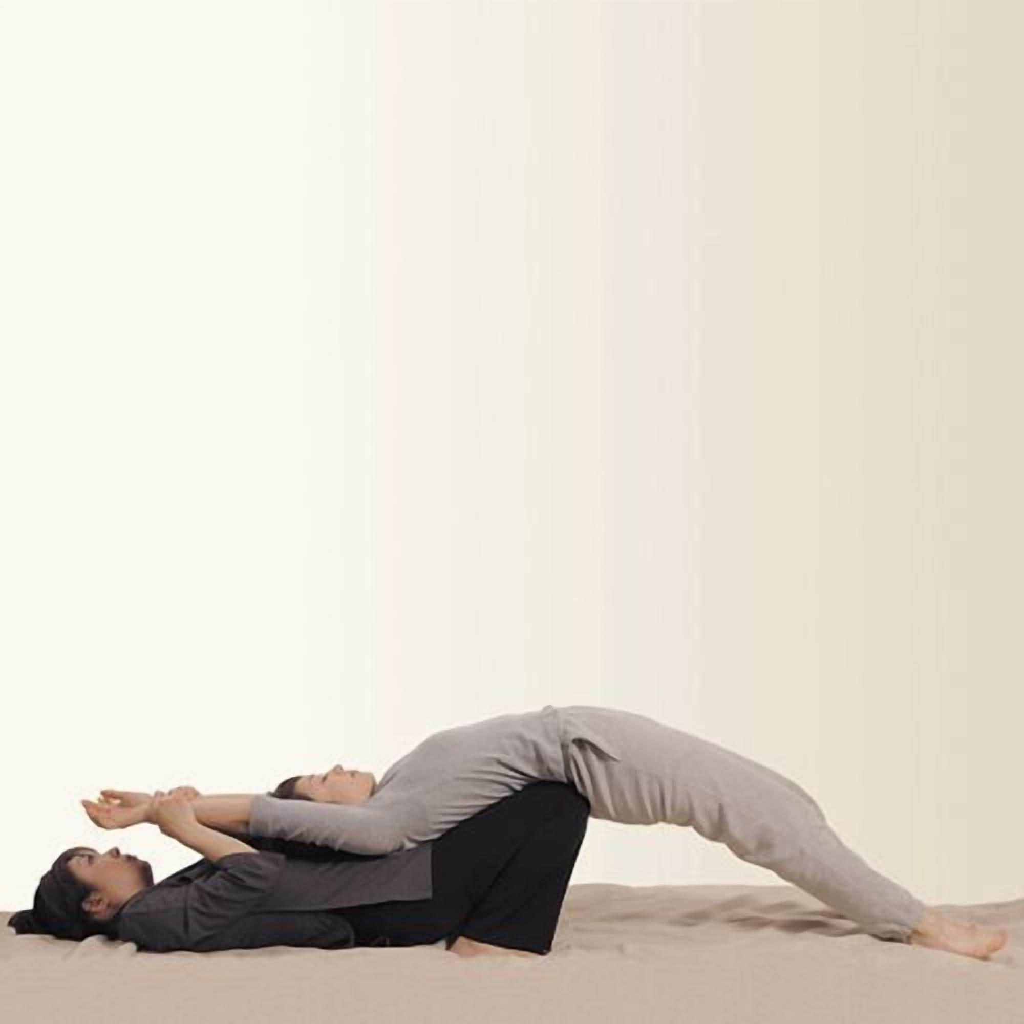 Two people performing a yoga pose on a plain floor.