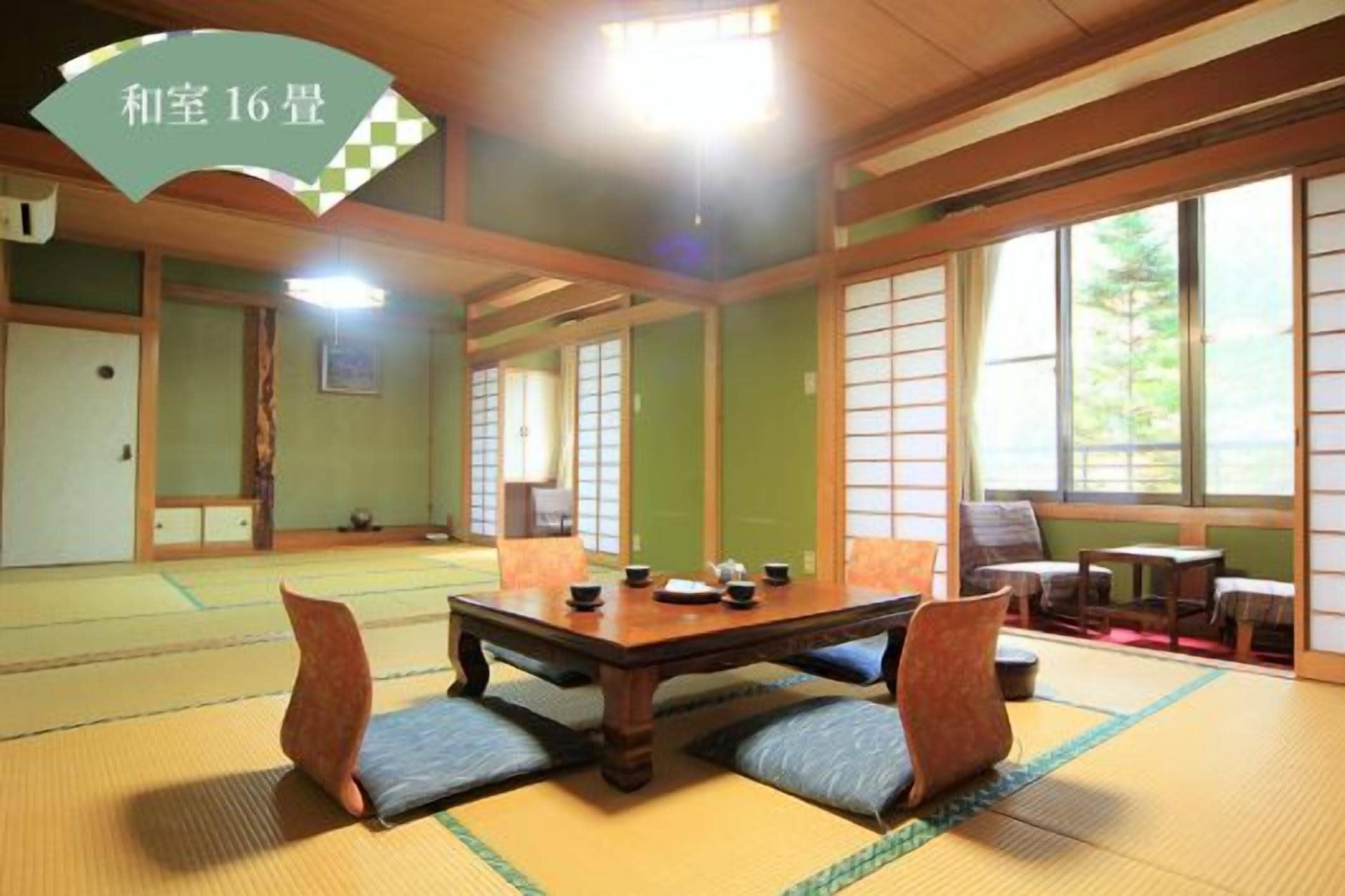 Una habitación japonesa tradicional con suelo de tatami, una mesa baja con cojines y puertas correderas.