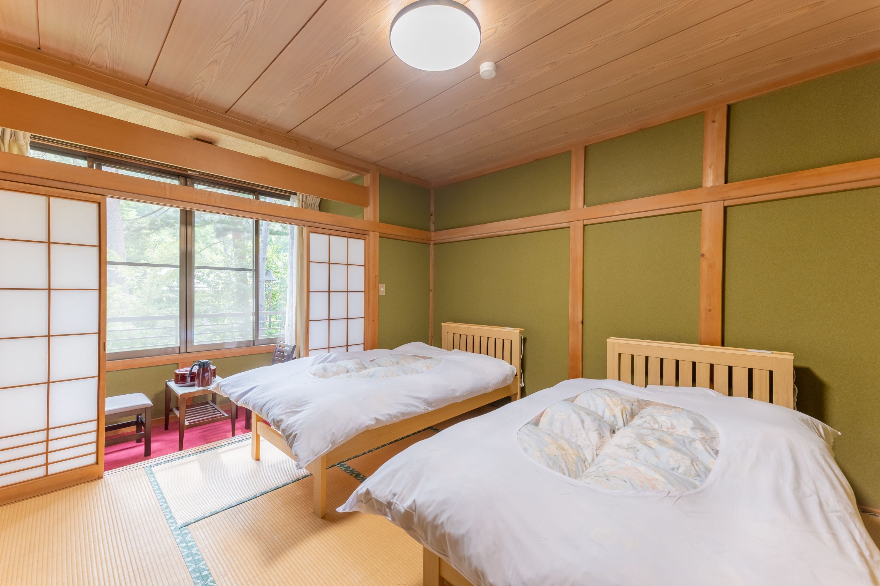 A traditional Japanese-style room with two beds, tatami mats, shoji screens, and a view of greenery outside.
