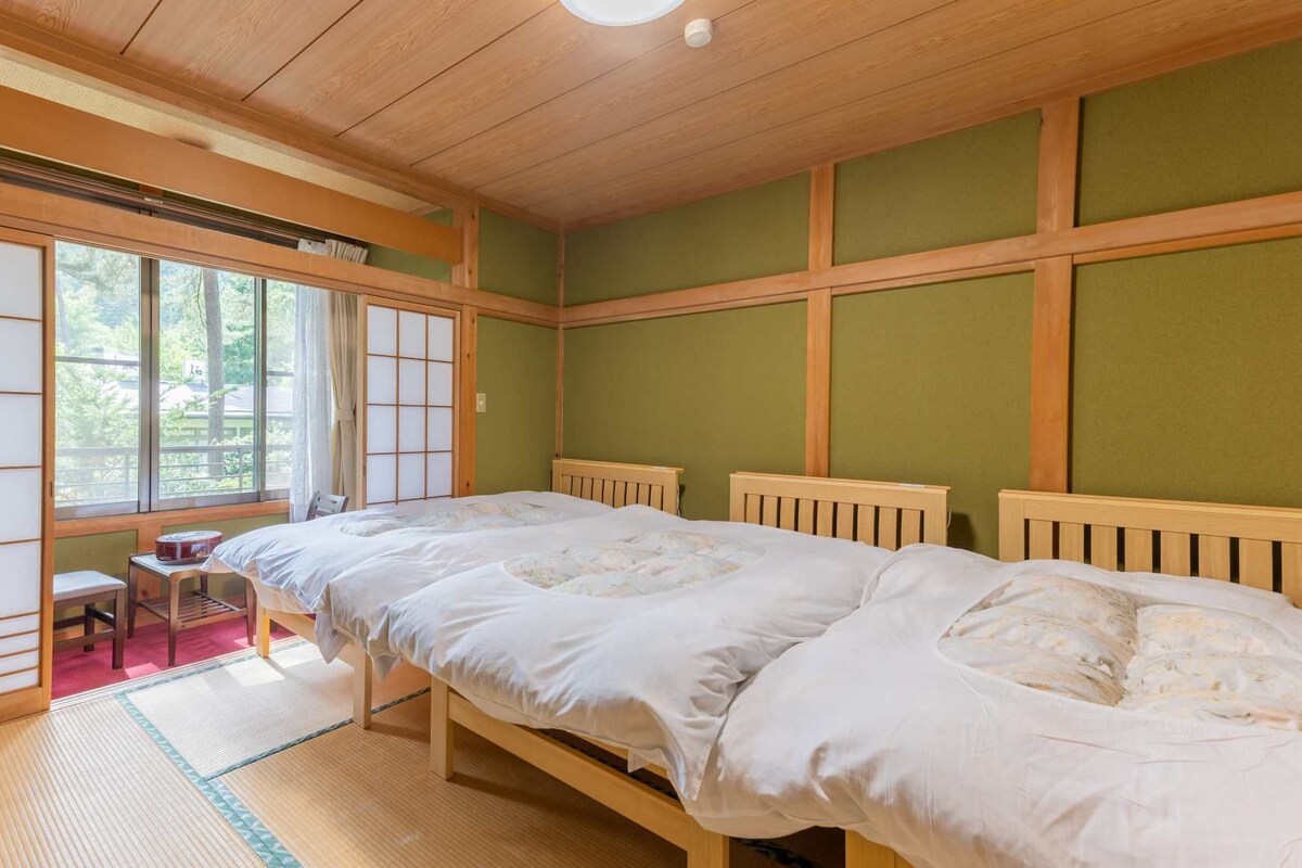 Un dormitorio de estilo japonés tradicional con suelo de tatami, futón, una mesita pequeña y un panel corredero shoji.