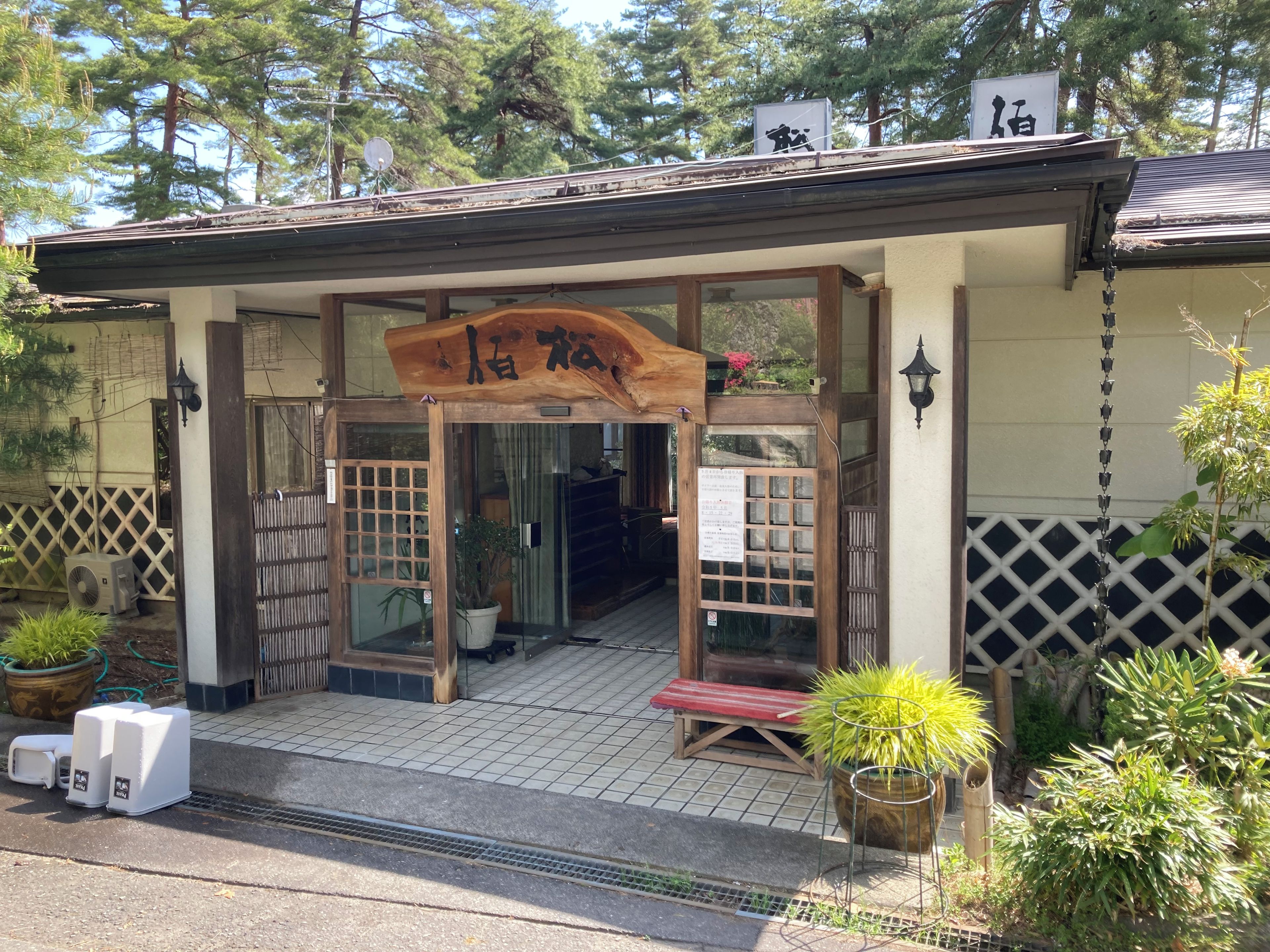 A traditional Japanese-style building with a wooden entrance, a signboard, and potted plants.