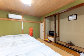 A traditional Japanese-style room with tatami flooring, a bed with white bedding, a television on a wooden stand, and a sliding door. - Shohaku (Azumino)