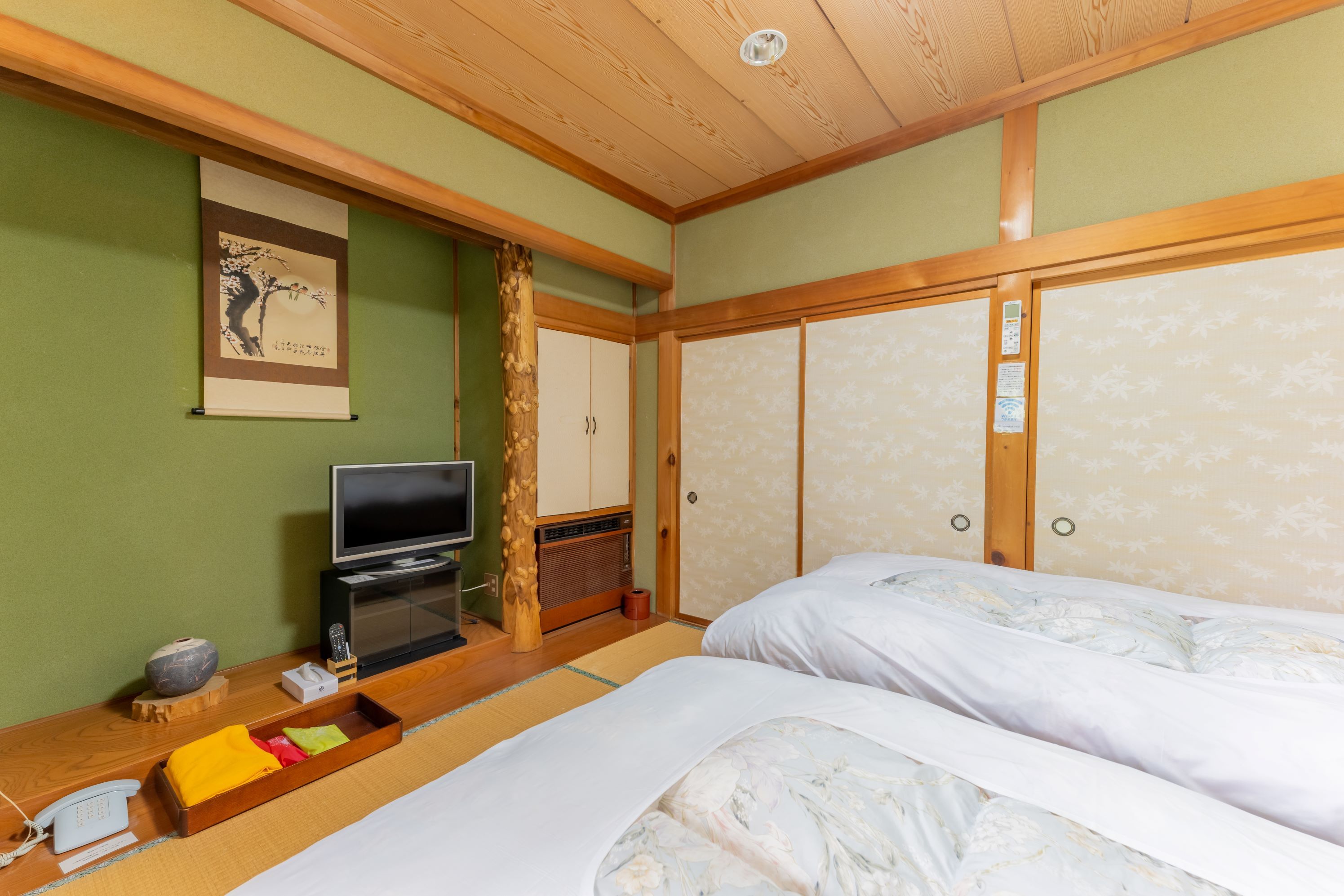 A traditional Japanese-style room with tatami flooring, a television, a wooden cabinet, and a bed with floral bedding.