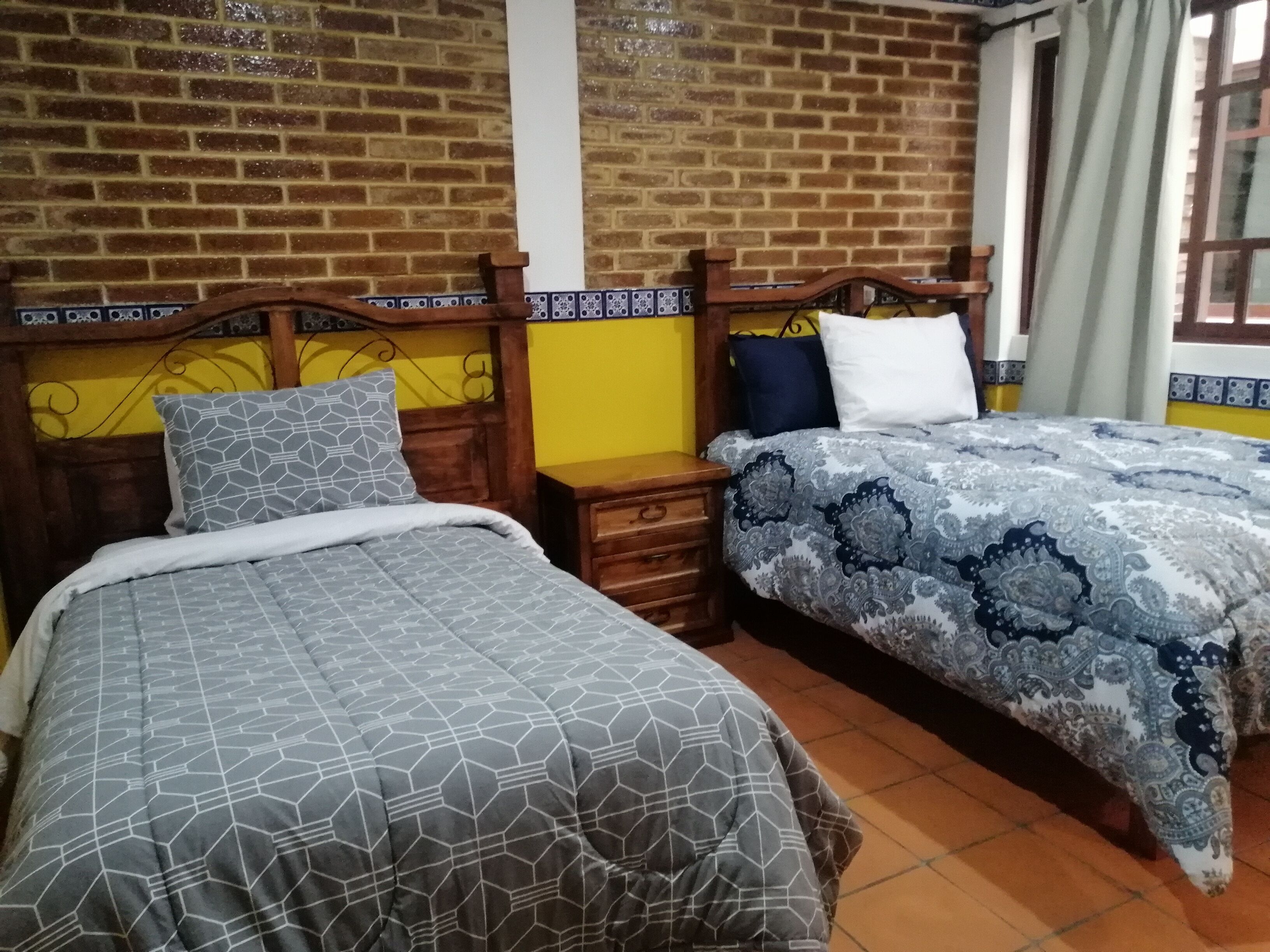 A room with two beds, each with a wooden headboard and patterned bedding.