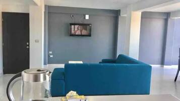 Un salon moderne avec un canapé bleu, une machine à café et un téléviseur fixé au mur.
