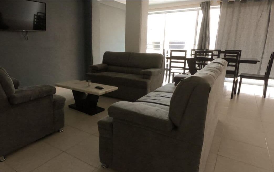 A living room with a sofa set, a coffee table, and a TV mounted on the wall.