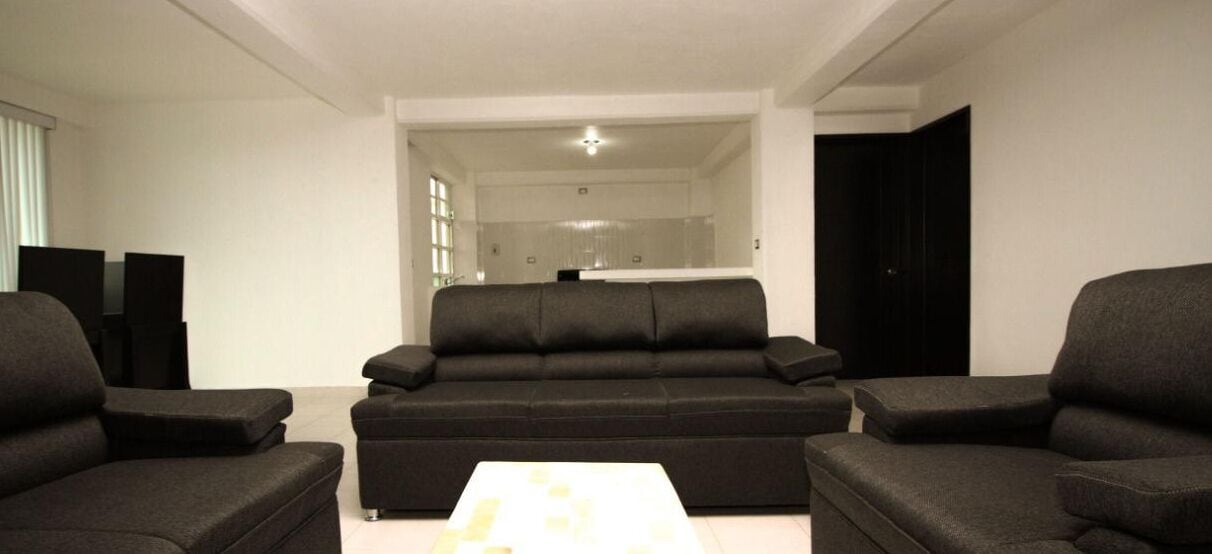 A modern living room with a black sofa set, a coffee table, and a TV on the left.