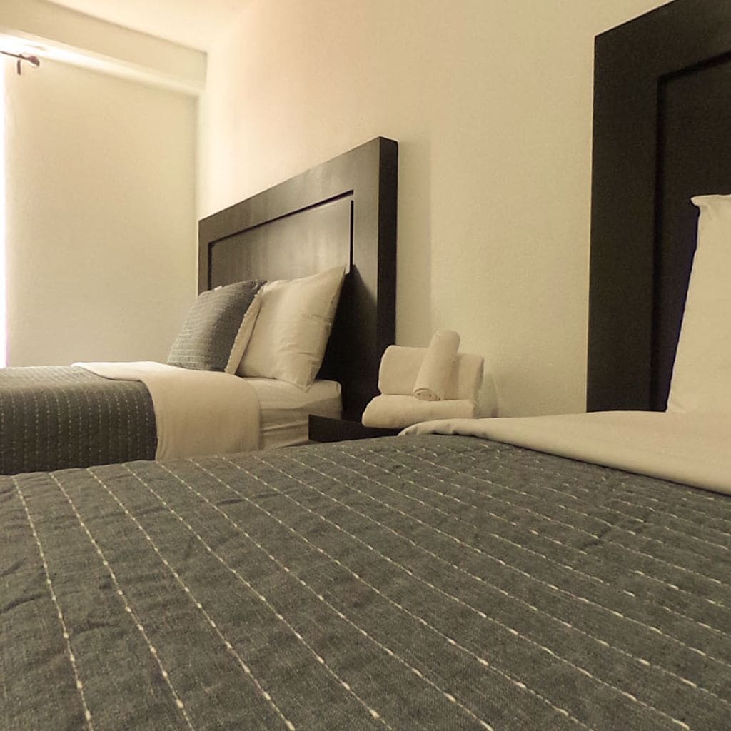 A hotel room with two beds, a dark headboard, and a white wall.