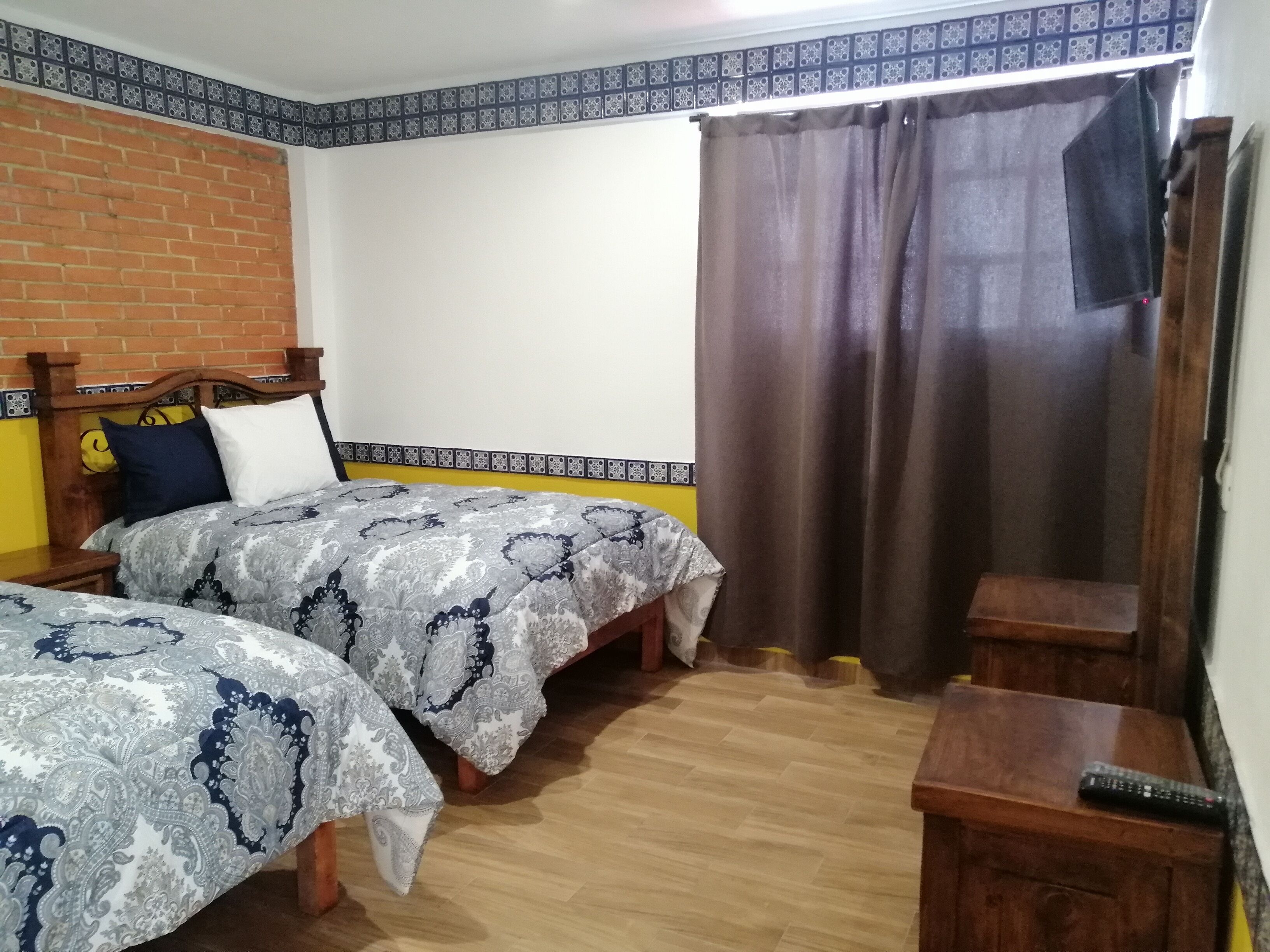 Un dormitorio con dos camas, una pared de ladrillo, un borde estampado y una cortina.