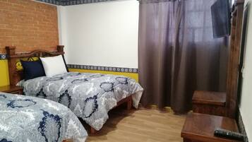 Un dormitorio con dos camas, una pared de ladrillo, un borde estampado y una cortina.