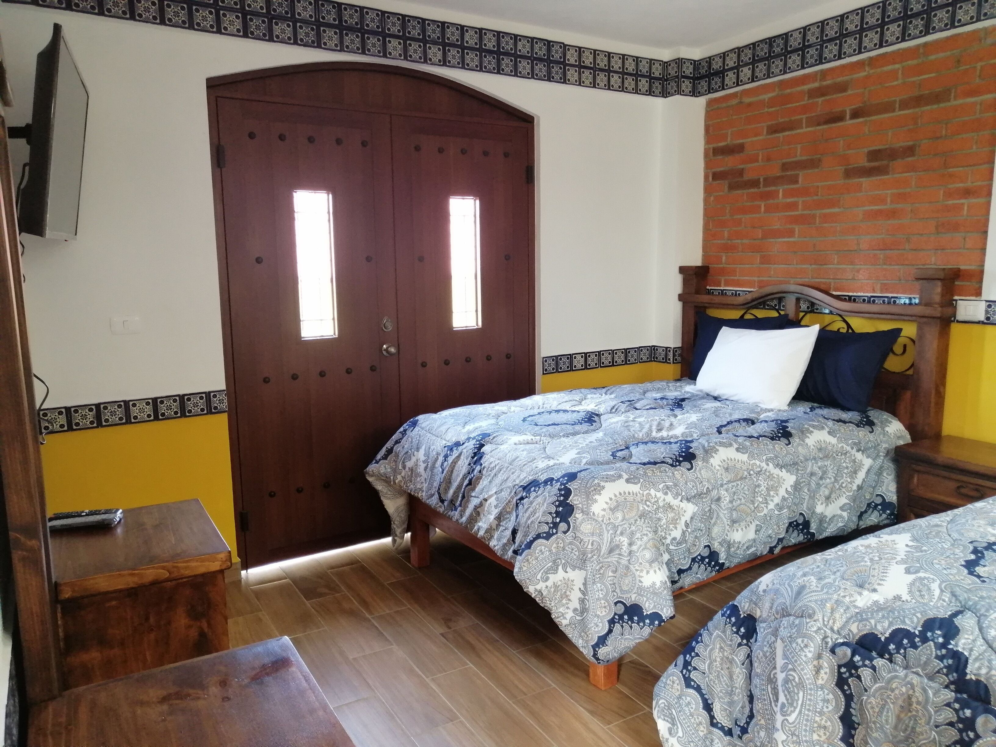 A bedroom with two beds, a wooden door, and a brick wall.
