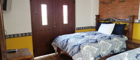 A bedroom with two beds, a wooden door, and a brick wall.