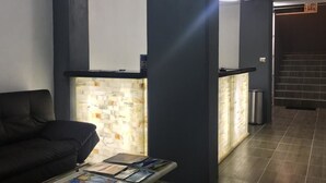 A reception area with a black sofa, a glass-top table with magazines, and a tiled wall with a light fixture. - Hotel y Suites Axolotl (Chignahuapan)