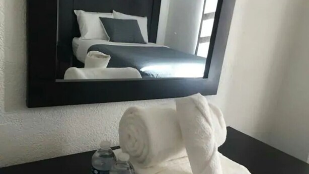 A hotel room with a bed, a mirror, a towel, and a bottle of water on a table. - Hotel y Suites Axolotl (Chignahuapan)