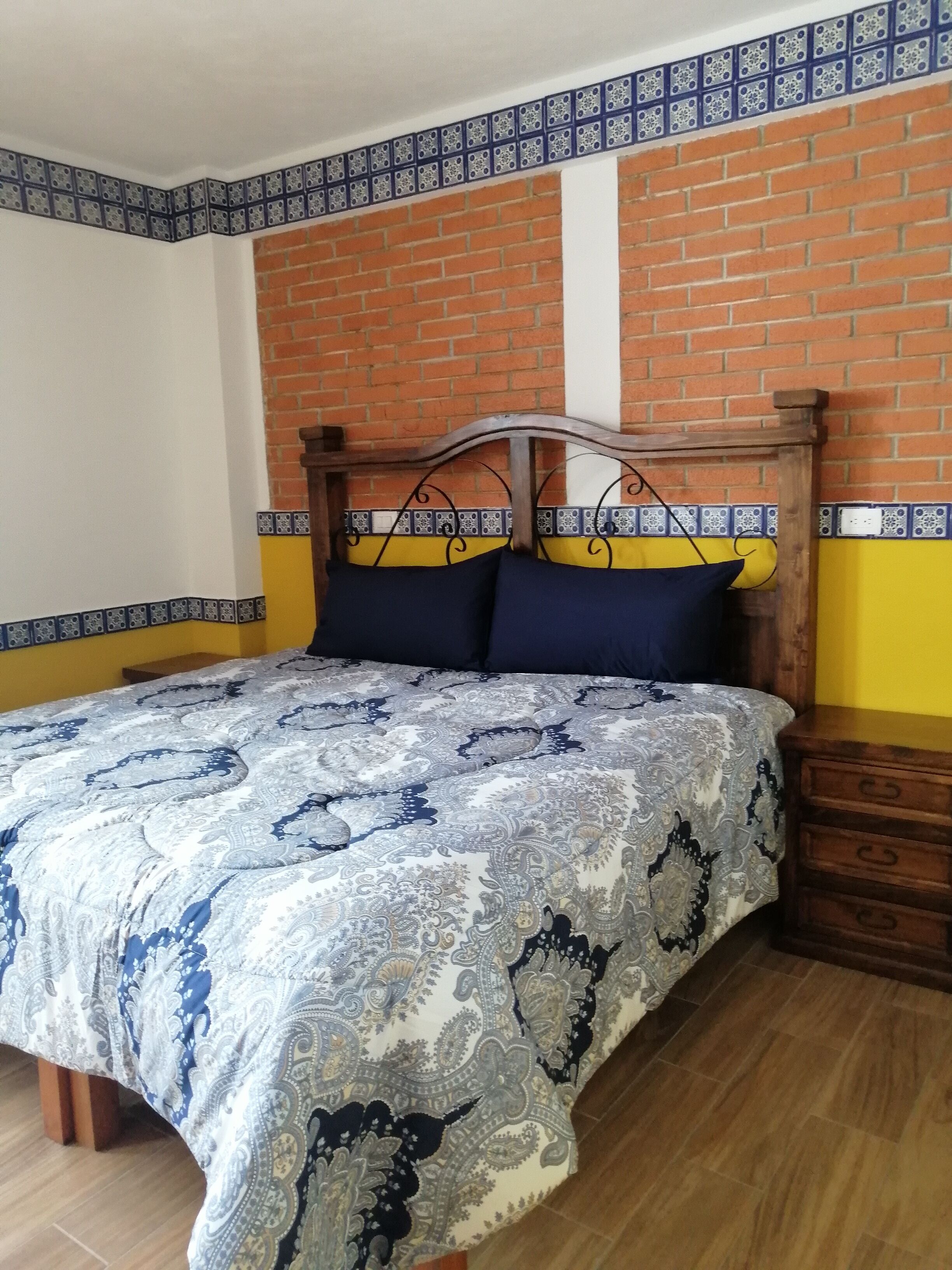 Una cama con colcha estampada, cabecero de madera y mesita de noche con cajones.